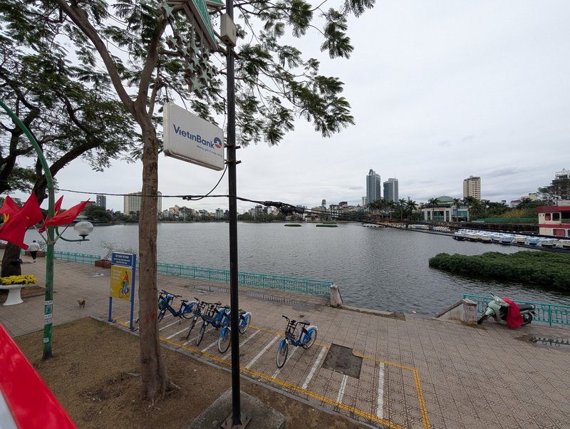 Piste cyclable et vue panoramique sur le lac de l’Ouest à Hanoï avec les immeubles en arrière-plan.