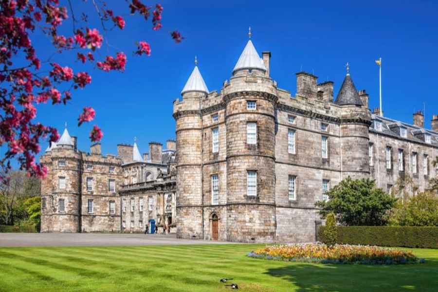 Le Palace of Holyroodhouse à Édimbourg, résidence officielle du roi en Écosse, entouré de cerisiers en fleurs.