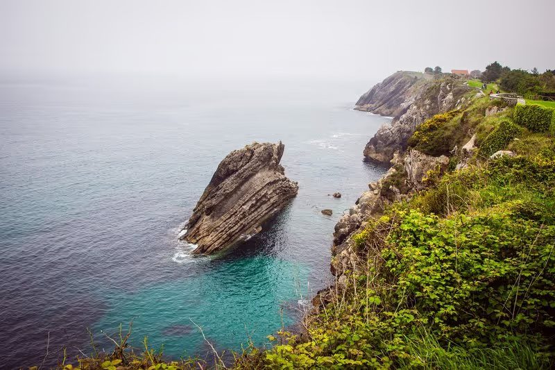 Côte rocheuse à Llanes avec une mer calme sous un ciel gris.