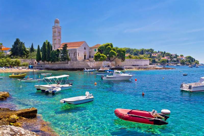 Bateaux flottant sur une eau turquoise à côté d'une église historique sur l'île de Hvar, Croatie.