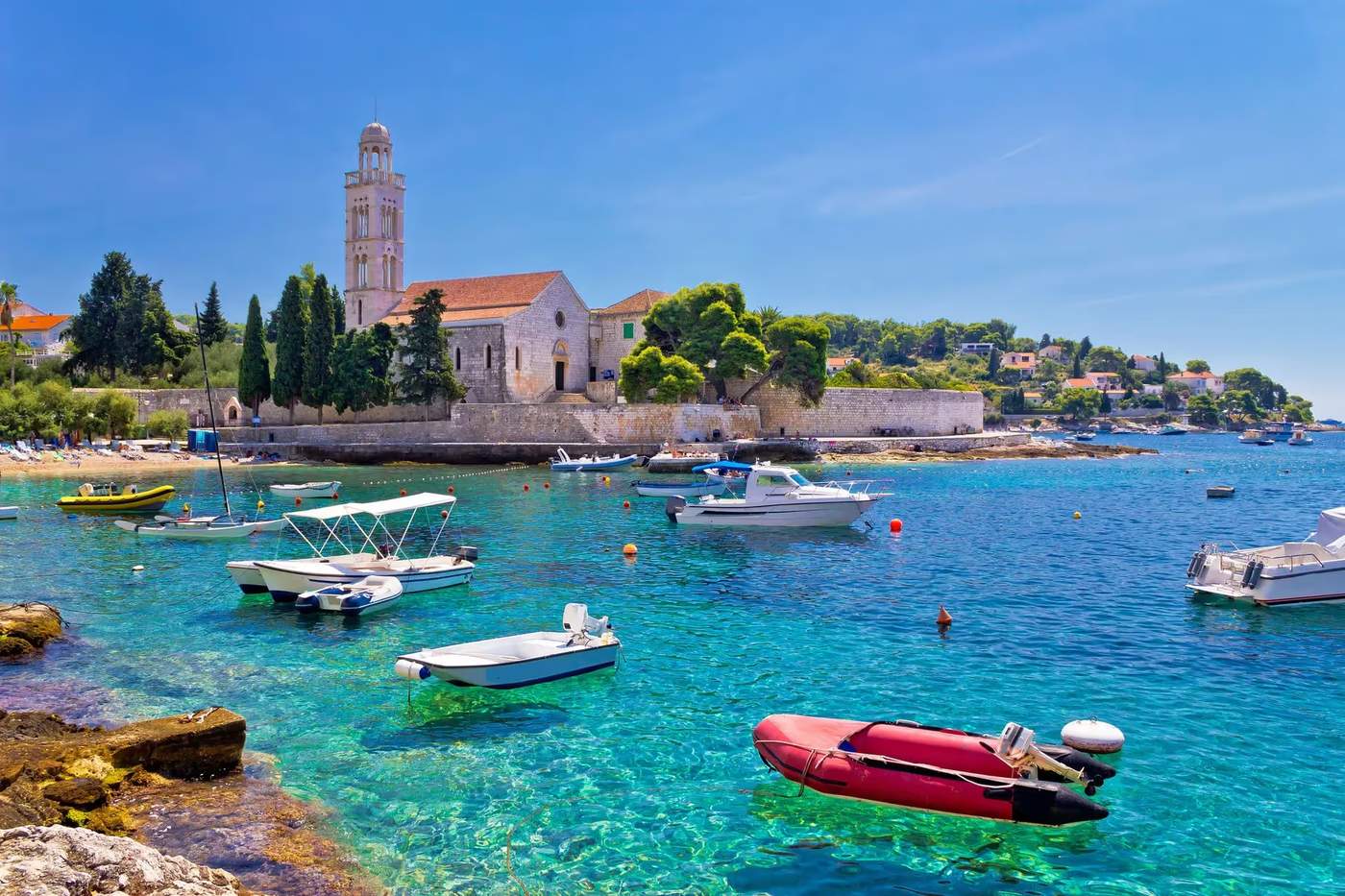 Bateaux flottant sur une eau turquoise à côté d'une église historique sur l'île de Hvar, Croatie.