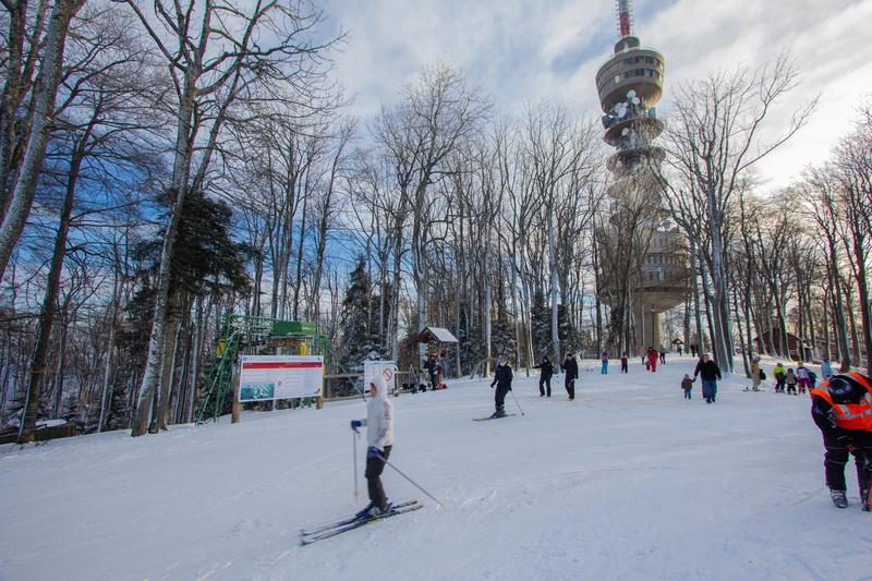 Piste de ski à Sljeme, entourée de forêts enneigées et avec une tour emblématique en arrière-plan.