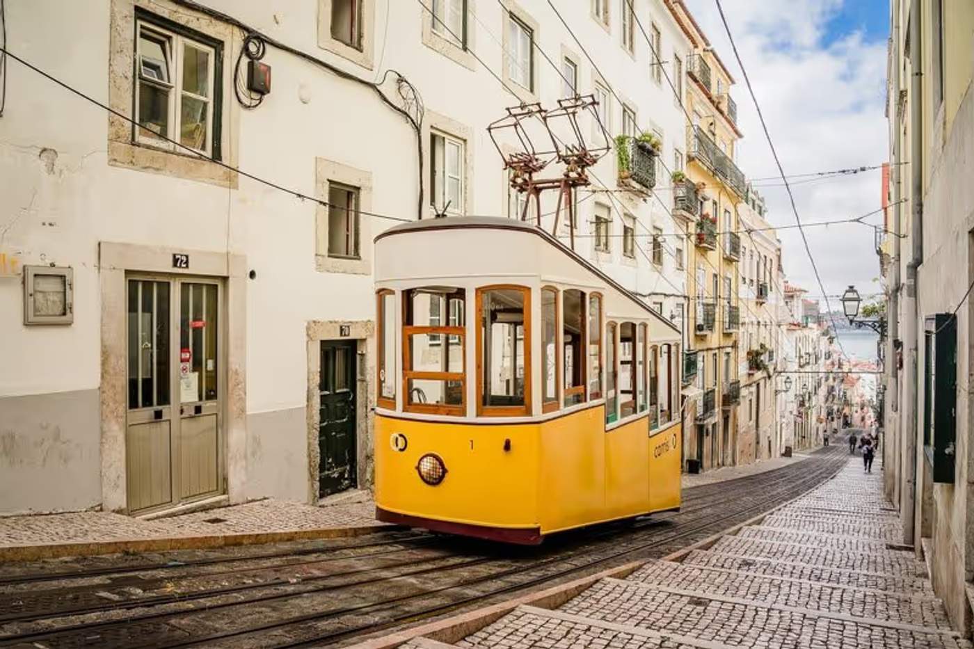 Tramway jaune typique roulant dans une rue pavée et étroite du centre historique de Lisbonne, Portugal.