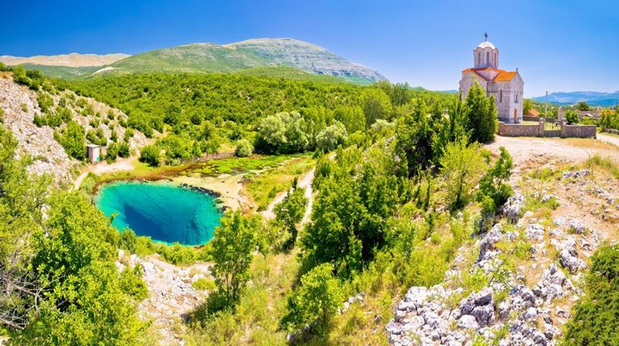 Vue panoramique de la source Cetina entourée de verdure avec une église à proximité.