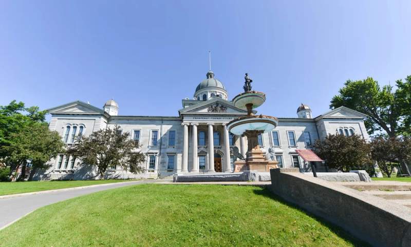 Façade du Frontenac County Court à Kingston avec sa fontaine historique et son architecture en pierre calcaire sous un ciel bleu.