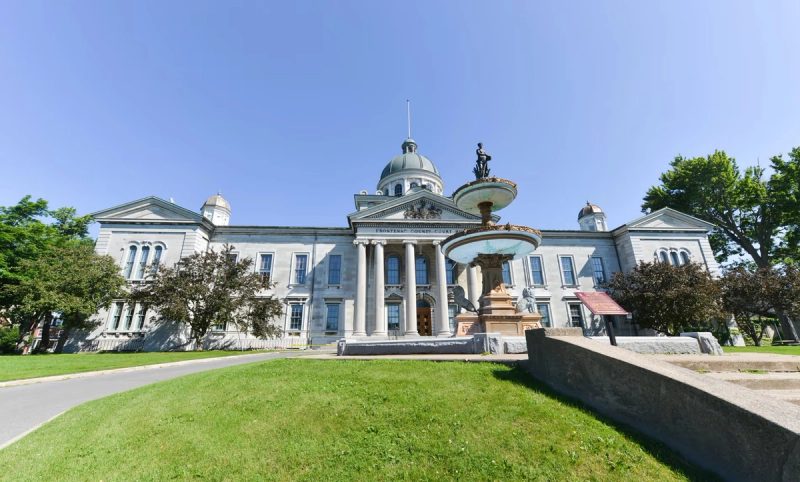 Façade du Frontenac County Court à Kingston avec sa fontaine historique et son architecture en pierre calcaire sous un ciel bleu.