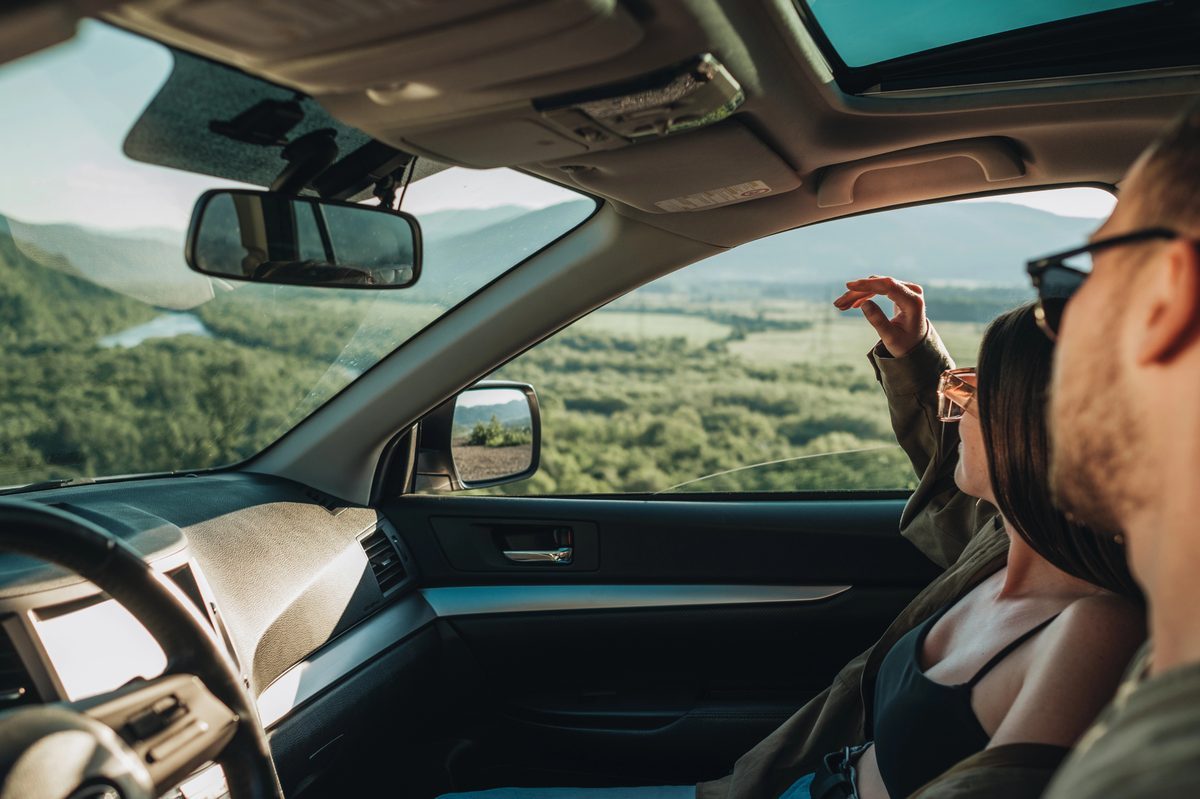 Couple dans une voiture de location admirant un paysage de vallée verdoyante en road trip