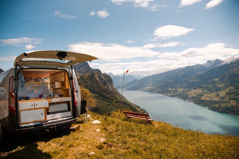 Van aménagé avec porte arrière ouverte face à un lac de montagne, illustrant un voyage en vanlife en pleine nature.