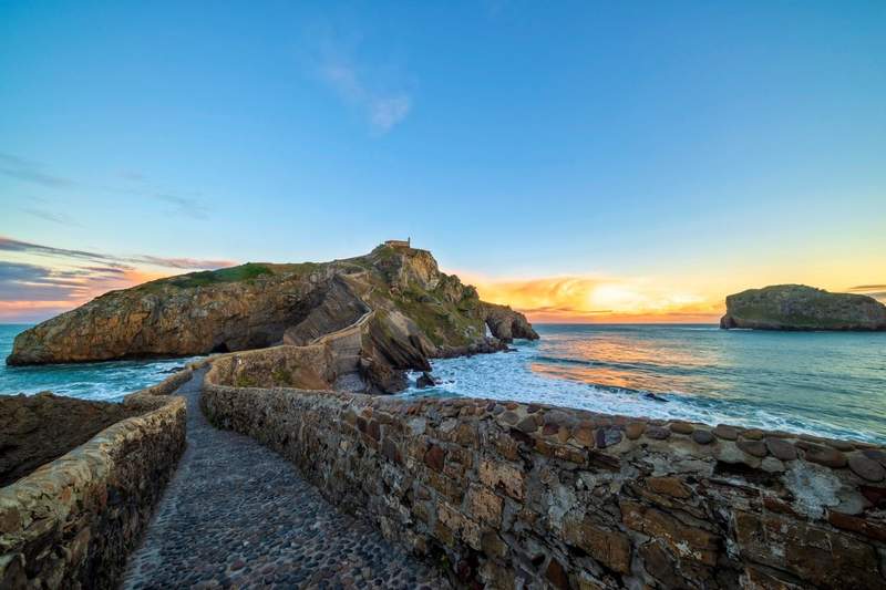 Pont de pierre menant à San Juan de Gaztelugatxe au coucher du soleil, îlot rocheux battu par les vagues sur la côte du Pays basque espagnol.