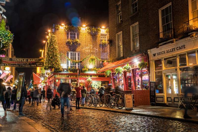 Vue nocturne animée du quartier de Temple Bar à Dublin, avec des lumières festives et des passants appréciant la vie nocturne.