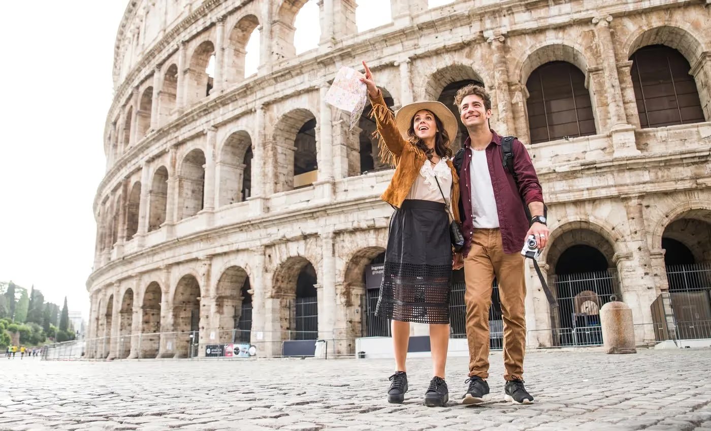Couple de voyageurs souriants visitant le Colisée à Rome, tenant une carte et un appareil photo.