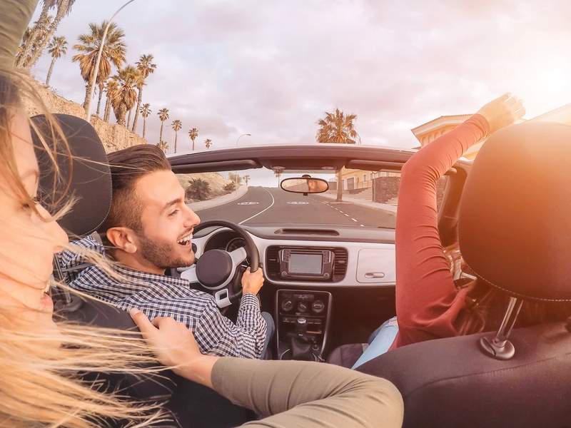 Amis en road trip au volant d'un cabriolet décapotable, route bordée de palmiers
