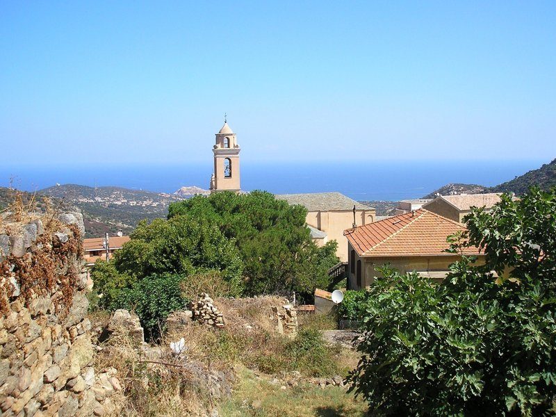 Vue sur un village perché typique de la Balagne avec la mer en arrière-plan.