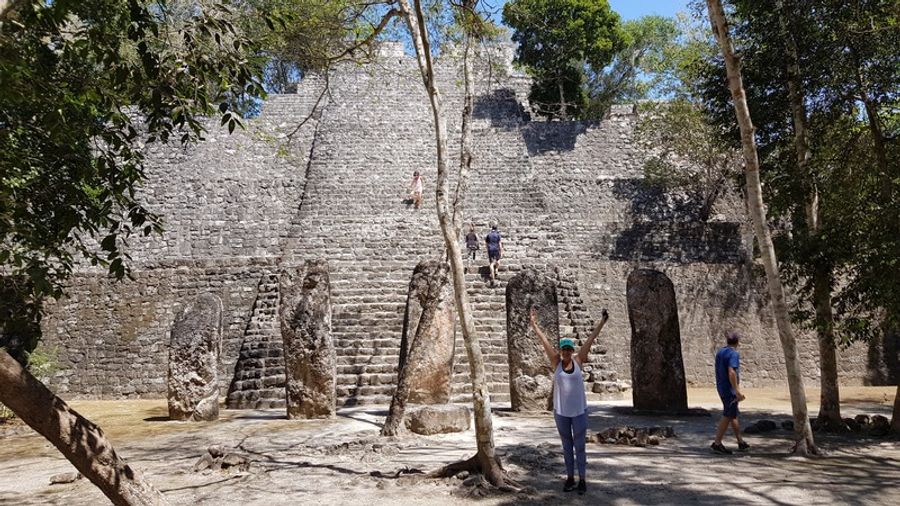 Une femme debout devant un temple maya recouvert de mousse et de racines, au cœur de la jungle de Calakmul