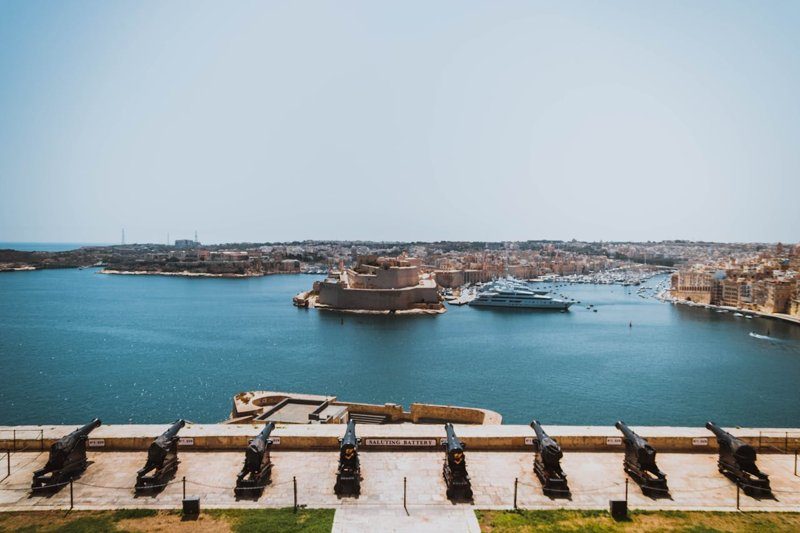 Vue depuis la Saluting Battery à La Valette, Malte, avec des canons alignés surplombant le Grand Harbour et une ancienne forteresse en contrebas.