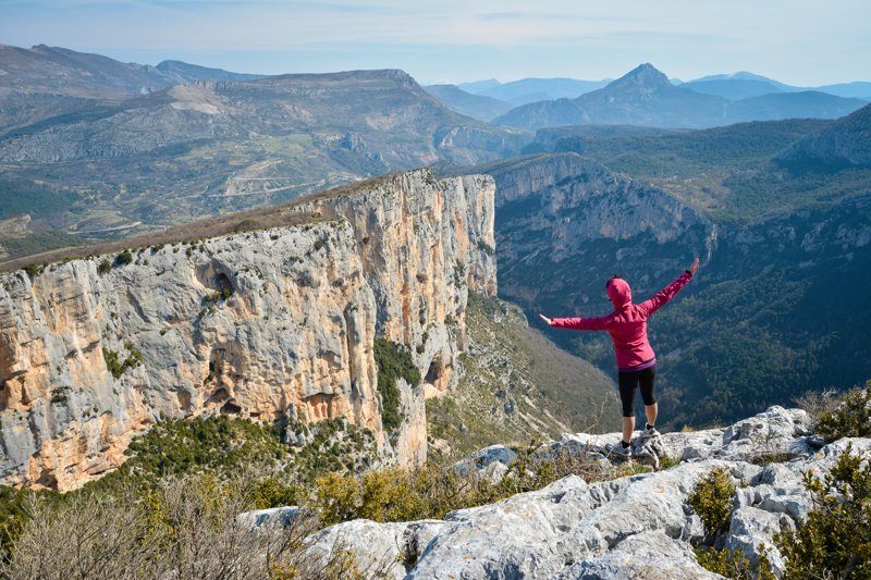 Une randonneuse sur un sommet rocheux avec une vue spectaculaire sur les falaises des Gorges du Verdon.