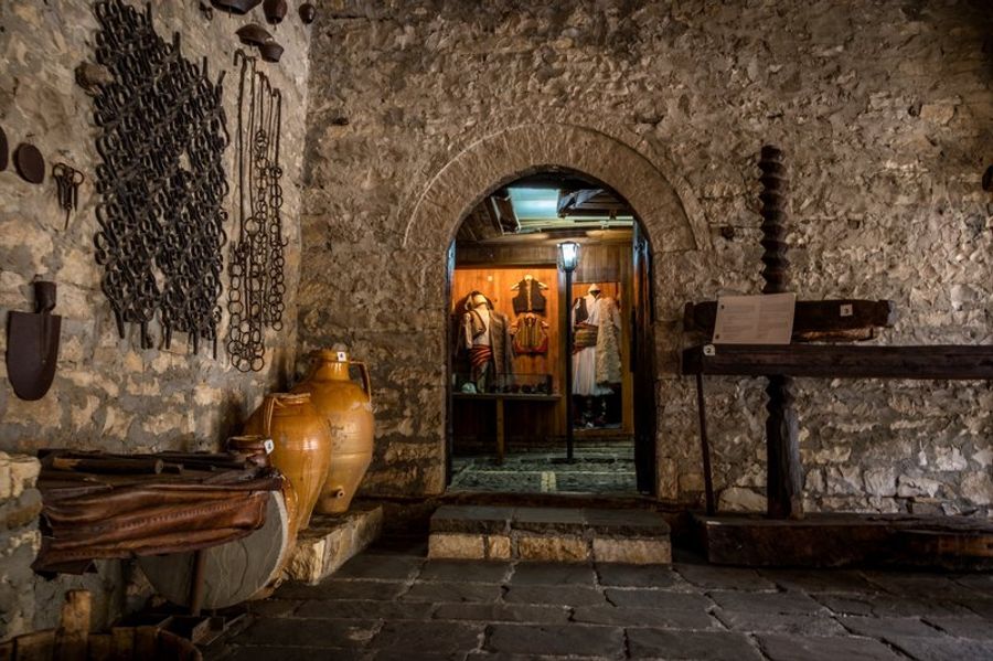 Intérieur du musée ethnographique de Berat, présentant des objets traditionnels albanais et des costumes historiques dans un cadre en pierre.
