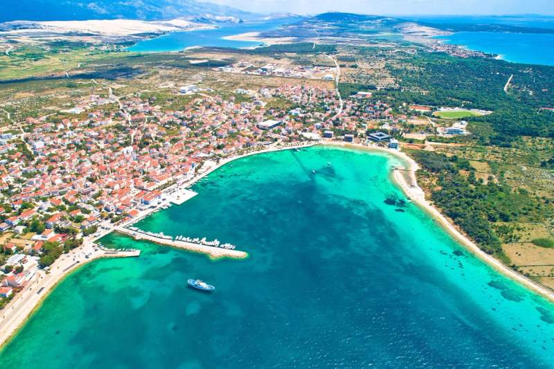 Vue aérienne de la ville côtière de Pag en Croatie, avec ses eaux turquoise et ses plages bordées de maisons colorées.
