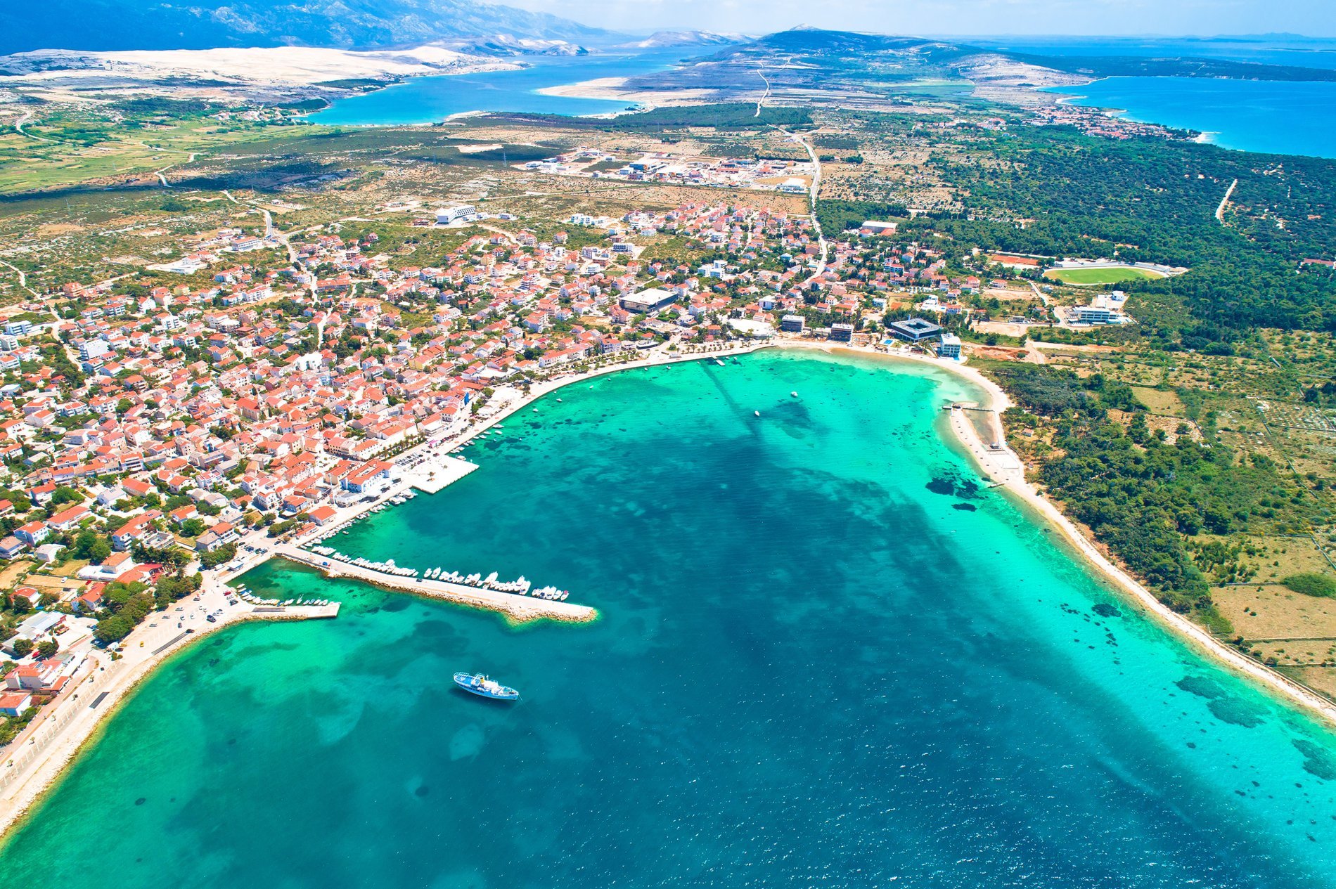 Vue aérienne de la ville côtière de Pag en Croatie, avec ses eaux turquoise et ses plages bordées de maisons colorées.