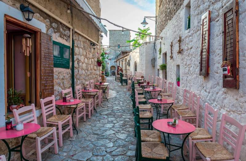Une ruelle pavée avec des tables et chaises colorées d'un café en plein air à Areopoli, Grèce.