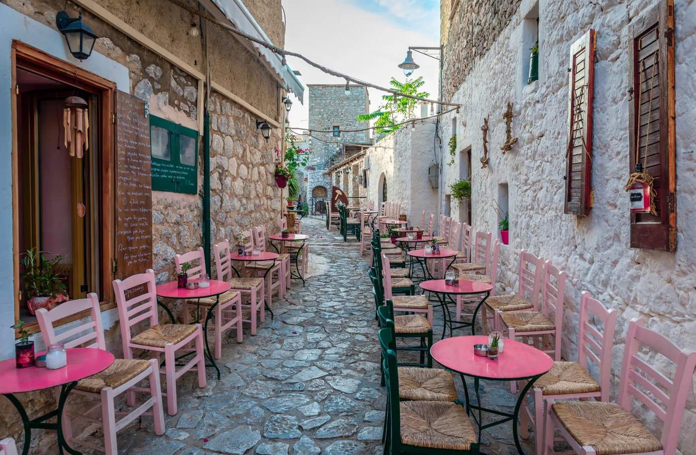 Une ruelle pavée avec des tables et chaises colorées d'un café en plein air à Areopoli, Grèce.