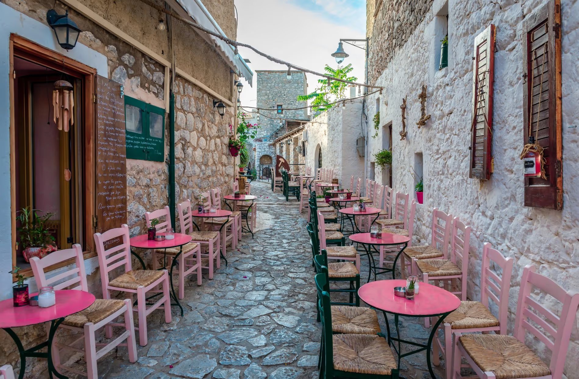 Une ruelle pavée avec des tables et chaises colorées d'un café en plein air à Areopoli, Grèce.