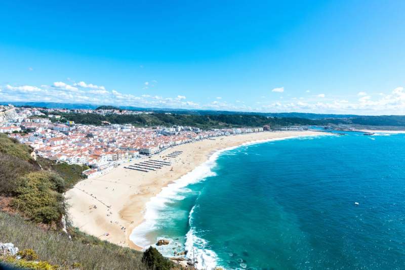 Vue panoramique de la plage de Nazaré, Portugal, avec ses vastes étendues de sable et l'océan Atlantique en arrière-plan.