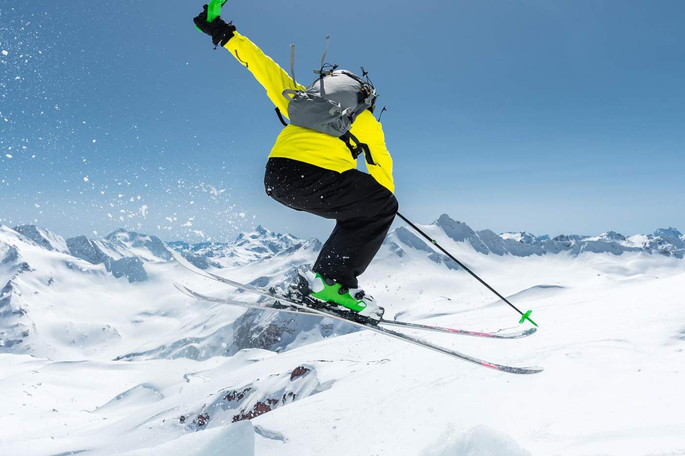 Skieur effectuant un saut spectaculaire au-dessus des montagnes enneigées, capturant l’adrénaline et la beauté des Alpes en pleine action.