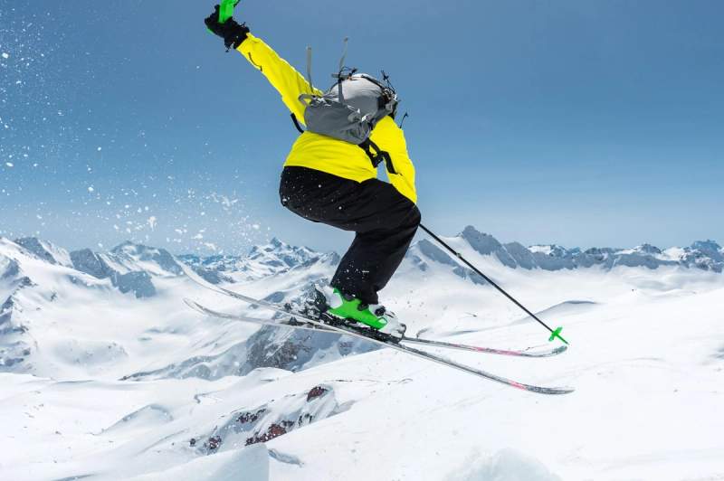 Skieur effectuant un saut spectaculaire au-dessus des montagnes enneigées, capturant l’adrénaline et la beauté des Alpes en pleine action.