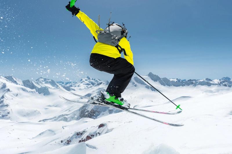 Skieur effectuant un saut spectaculaire au-dessus des montagnes enneigées, capturant l’adrénaline et la beauté des Alpes en pleine action.