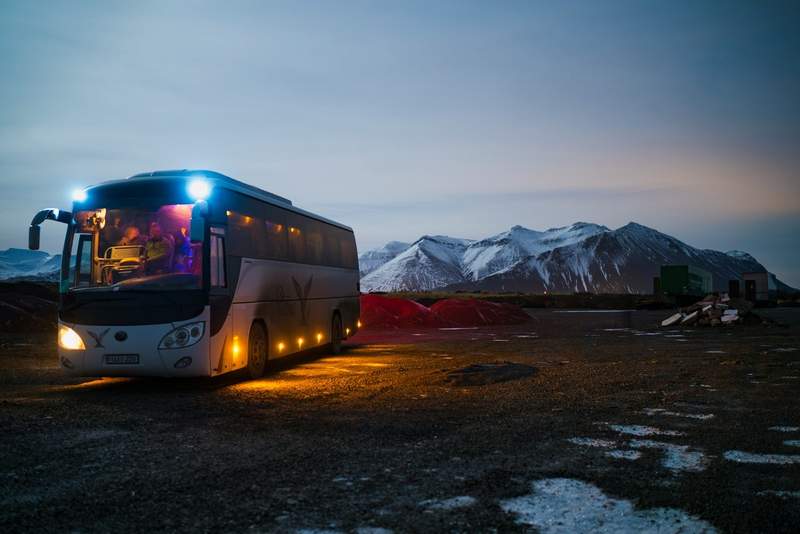 Bus touristique éclairé à la nuit tombée devant des montagnes enneigées en Islande