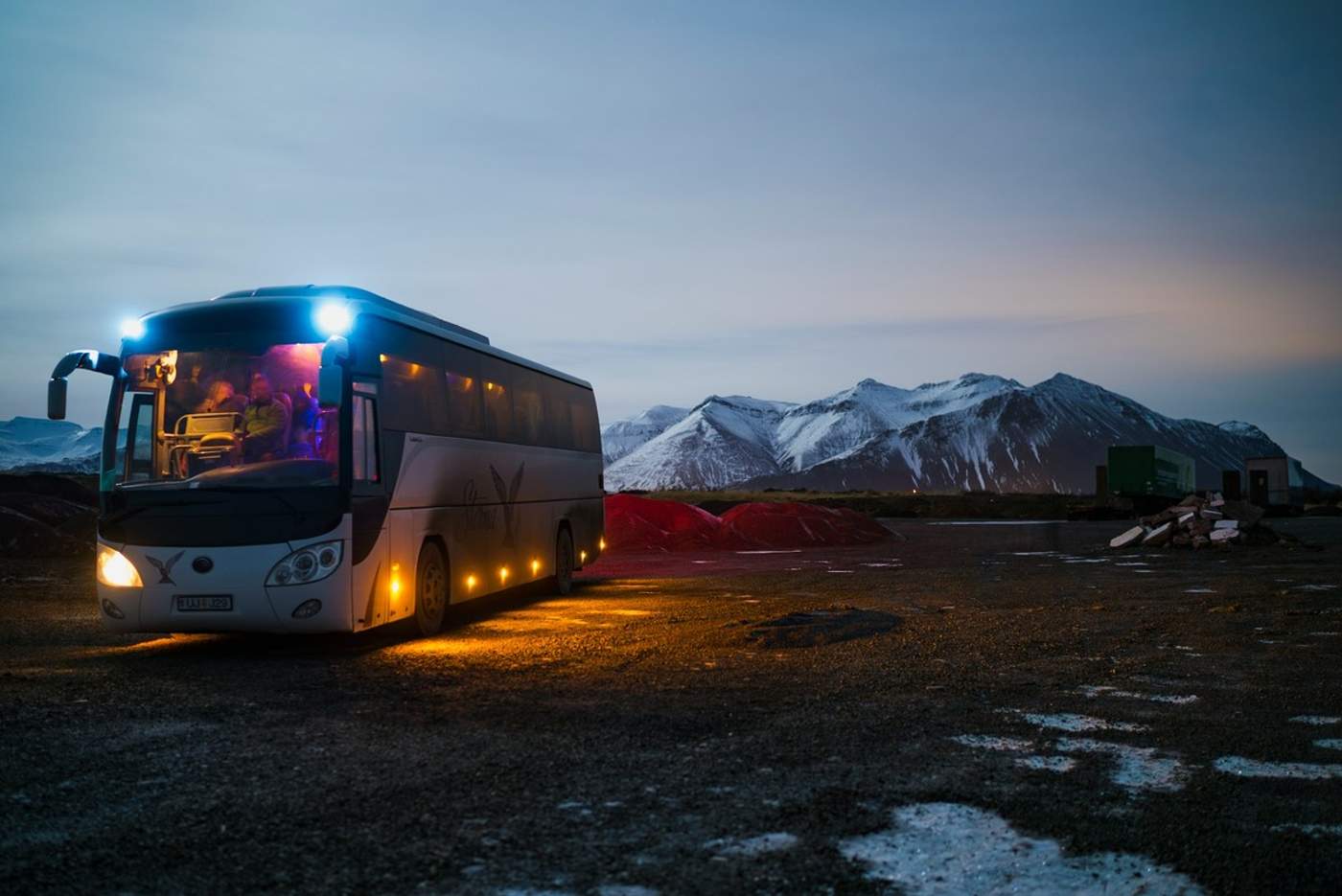 Bus touristique éclairé à la nuit tombée devant des montagnes enneigées en Islande