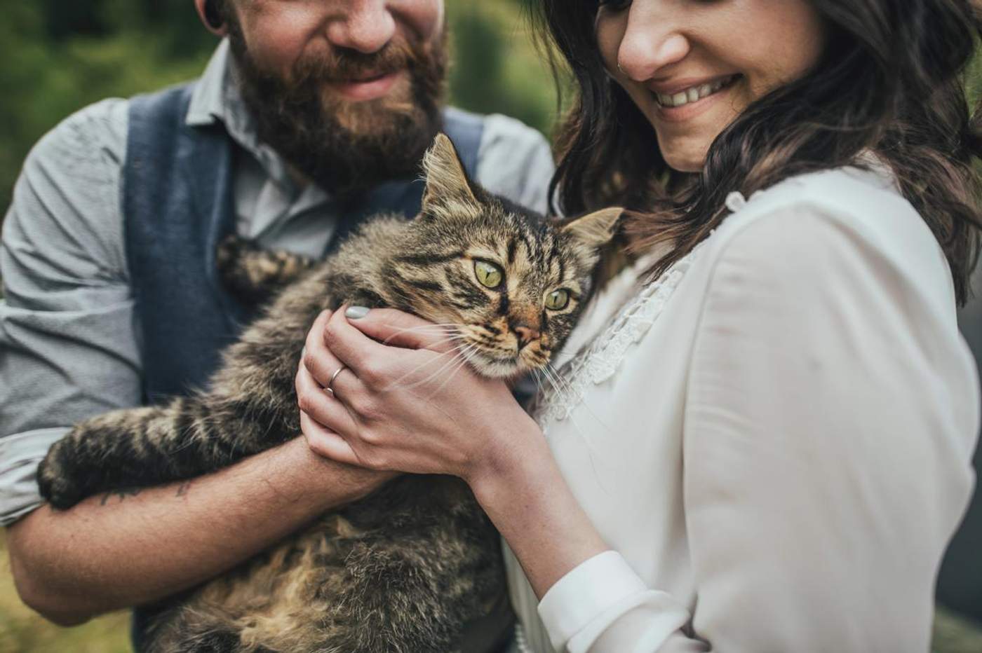 Couple souriant tenant un grand chat tigré dans les bras, moment tendre en extérieur