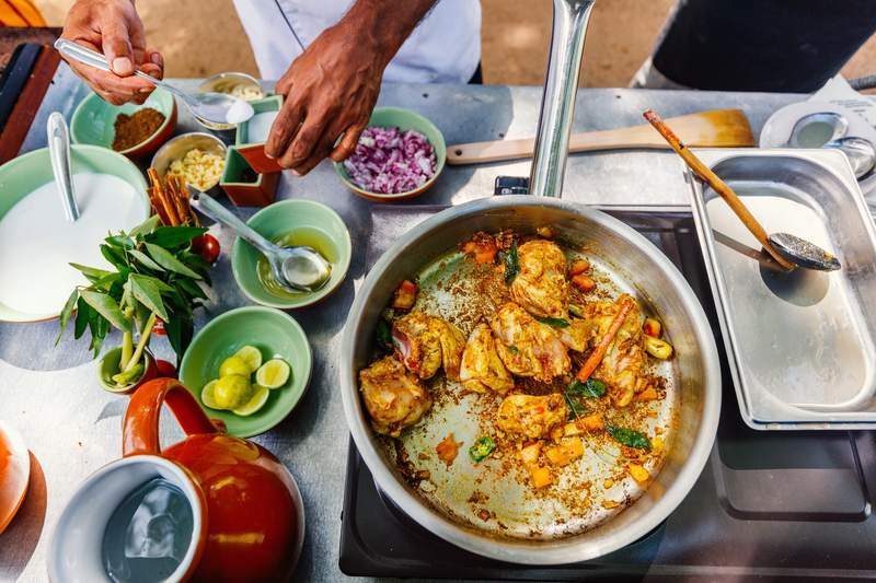 Préparation d’un curry sri-lankais dans une poêle avec épices et ingrédients frais.