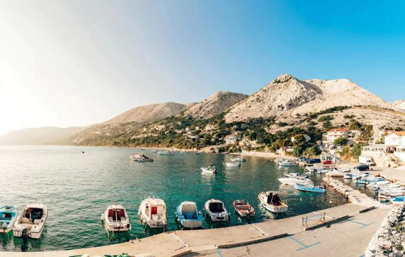 Image panoramique d'un port pittoresque à Krk, en Croatie, avec des bateaux amarrés et des montagnes en arrière-plan.