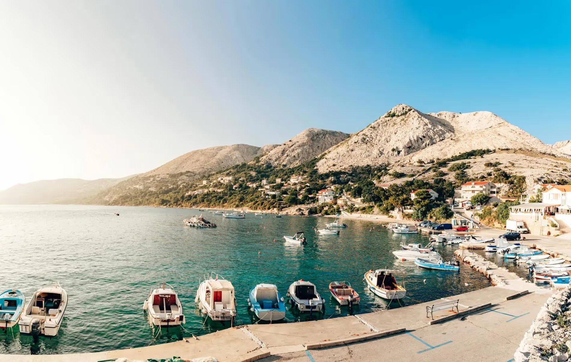 Image panoramique d'un port pittoresque à Krk, en Croatie, avec des bateaux amarrés et des montagnes en arrière-plan.