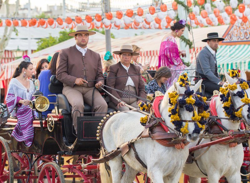 Groupe en costumes traditionnels andalous lors de la Feria de Abril, défilant sur une calèche tirée par des chevaux décorés de fleurs.