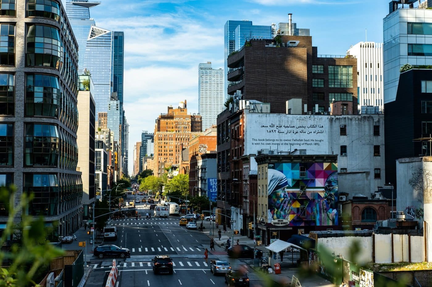 Vue animée d’une avenue à Manhattan bordée de gratte-ciel modernes et d’immeubles en briques, avec une fresque colorée au premier plan.