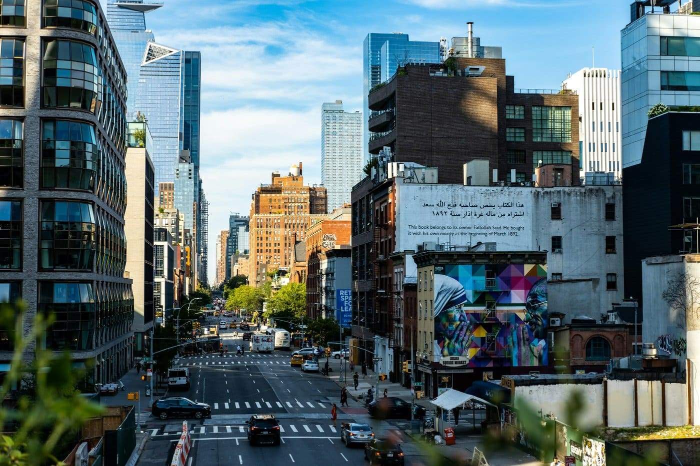 Vue animée d’une avenue à Manhattan bordée de gratte-ciel modernes et d’immeubles en briques, avec une fresque colorée au premier plan.