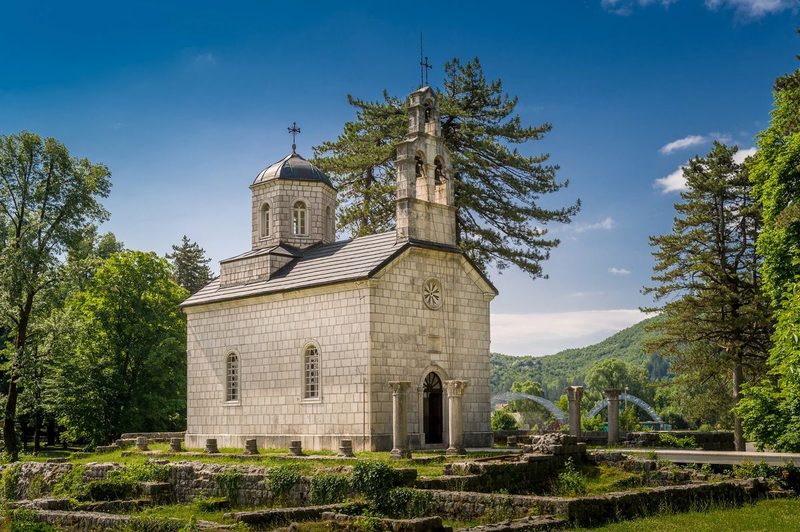 Église orthodoxe de la Cour Wallachienne à Cetinje, entourée de ruines et de pins, avec les montagnes du Monténégro en arrière-plan