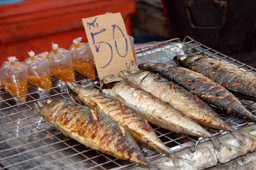Poissons grillés sur un marché de rue avec des sauces épicées emballées à proximité.