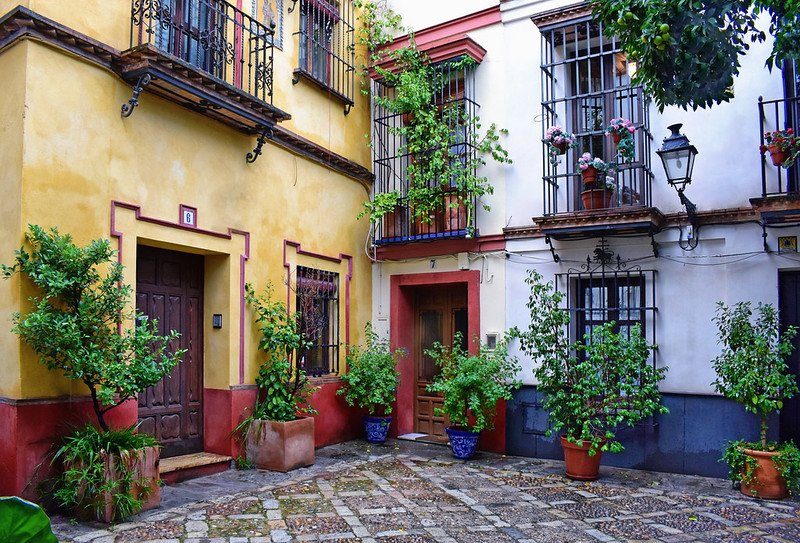 Une petite cour colorée dans le quartier de Santa Cruz, avec des maisons aux façades jaunes et rouges décorées de plantes grimpantes.