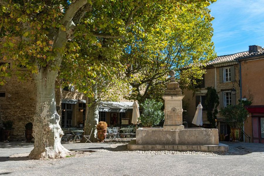 Fontaine pittoresque sur une place ombragée de Gordes, entourée de maisons provençales et de terrasses accueillantes.