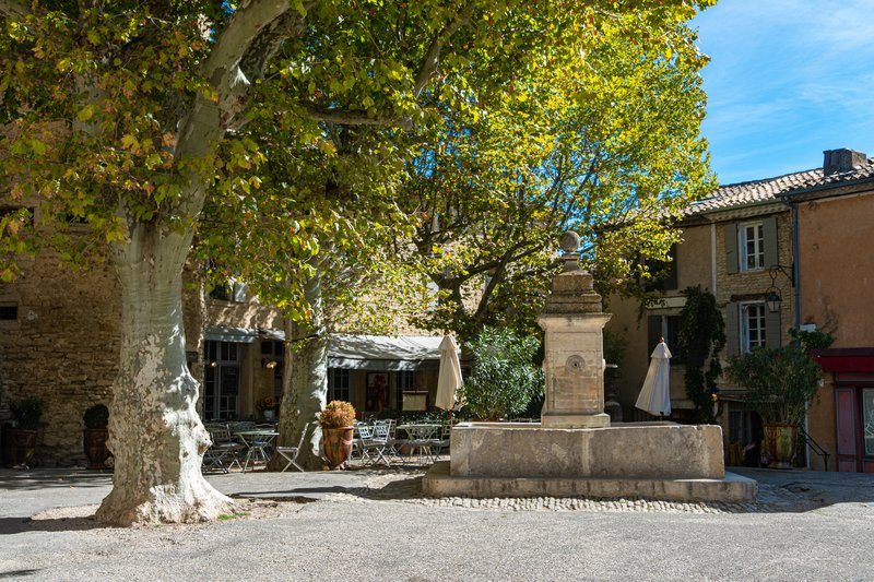 Fontaine pittoresque sur une place ombragée de Gordes, entourée de maisons provençales et de terrasses accueillantes.