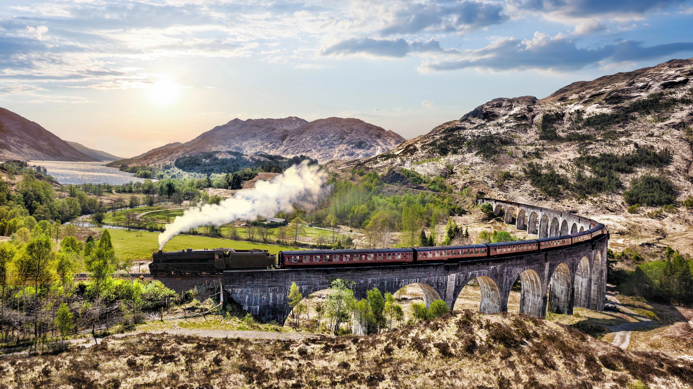 Le train à vapeur Jacobite traverse les arches du viaduc de Glenfinnan, avec les collines et le Loch Shiel à l’arrière-plan