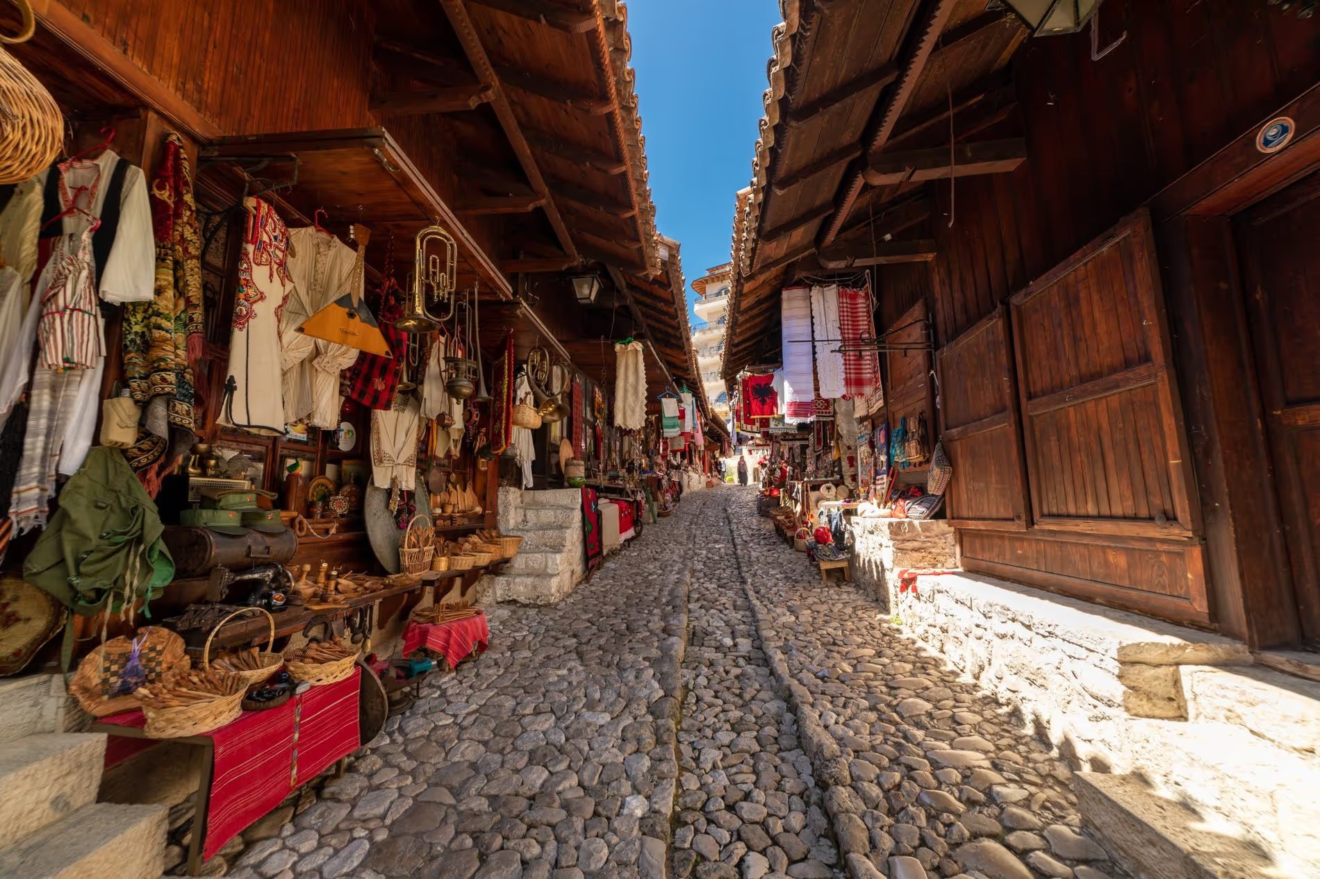 Rue pavée du bazar de Kruja avec boutiques d'artisanat albanais traditionnels exposant tissus, objets en cuivre et souvenirs.