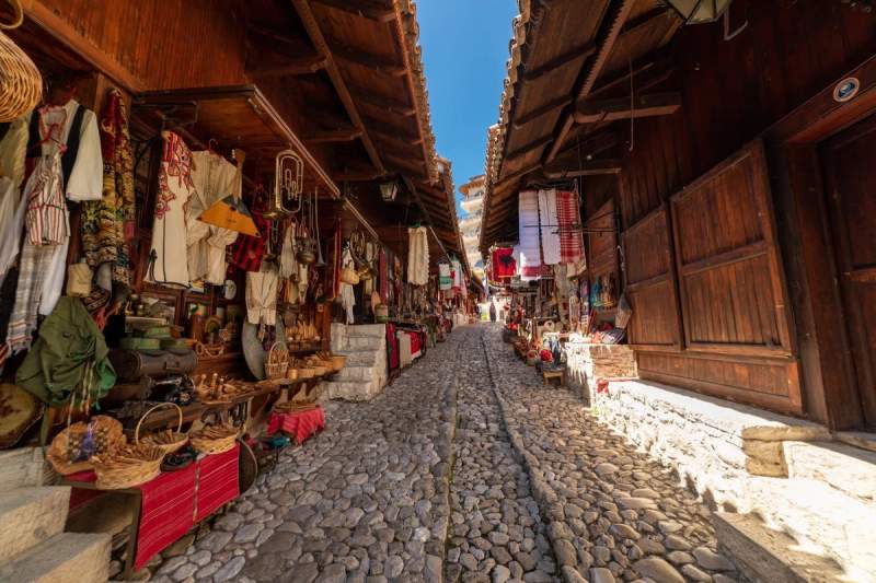 Rue pavée du bazar de Kruja avec boutiques d'artisanat albanais traditionnels exposant tissus, objets en cuivre et souvenirs.