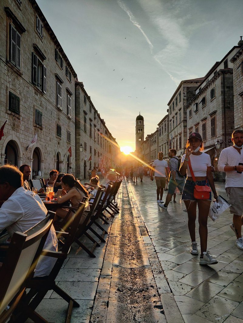 La Stradun, rue principale piétonne de la vieille ville de Dubrovnik, animée au coucher du soleil avec ses terrasses de cafés et sa lumière dorée se reflétant sur les pavés