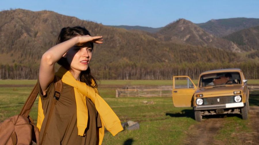 Femme en road trip devant des montagnes avec voiture vintage stationnée en pleine nature