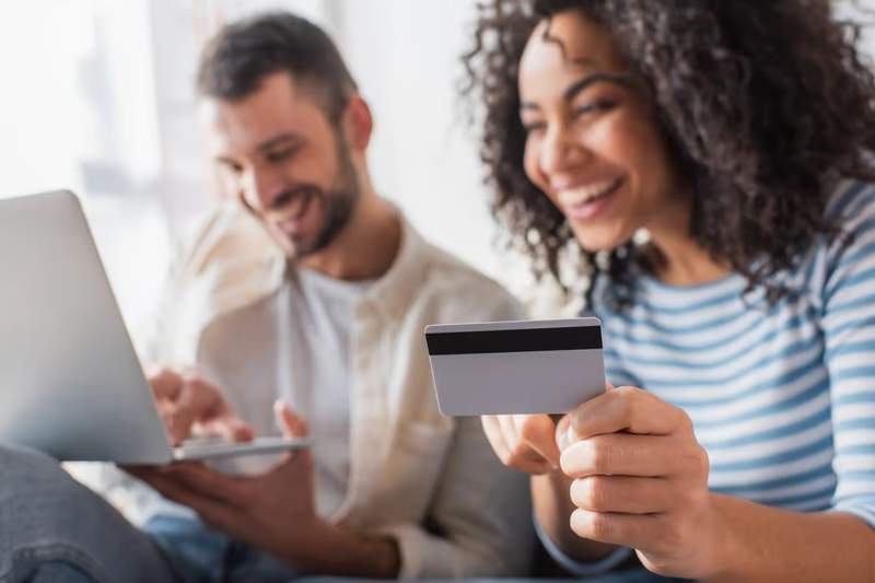 Couple souriant effectuant un paiement en ligne avec une carte bancaire sur un ordinateur portable